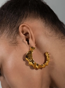 Close-up of chunky gold-plated C-shaped hoop earrings with textured ripple design