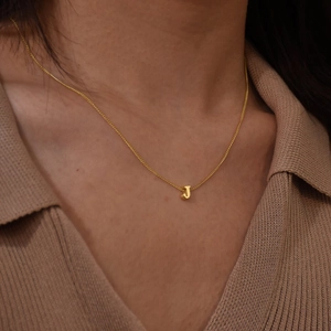 Close-up of golden bubble letter J pendant necklace on model with knit sweater