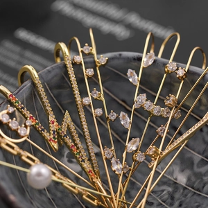 Golden piercing earrings set with shimmering zircons and pearls on grey ceramic tray