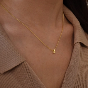 Close-up of a gold bubble letter J pendant on a delicate stainless steel chain necklace