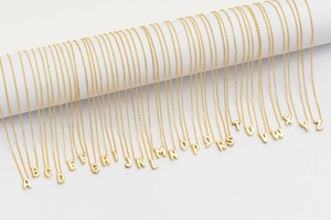 Macro display of 26 gold bubble alphabet initial necklaces on white cylinders