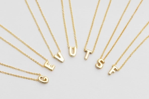 Macro shot of gold-plated alphabet bubble pendants G E V U T S F on minimalist chains