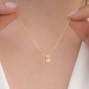 Close-up of a gold bubble letter G pendant necklace worn by a model for a stylish look
