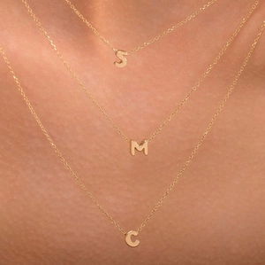 Macro detail of gold-plated layered chain necklaces with bubble letters S M and C
