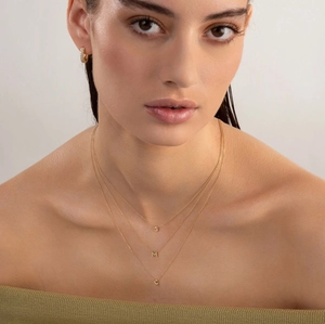 Close-up of golden bubble initial necklaces S M C and stud earrings on model