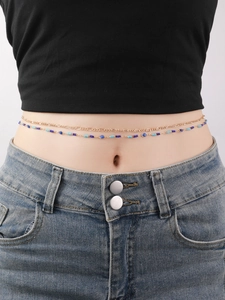 Close-up of double-layer gold waist chain with blue evil eye beads on a model