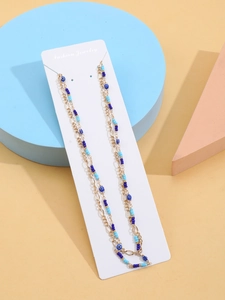 Close-up of double-layer gold chain with blue beads and evil eye pendants on jewelry card