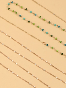 Detail of layered gold body chain with emerald green beads and sunburst metallic charms