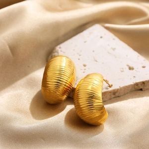 Macro shot of gold textured dome earrings on champagne silk and stone background
