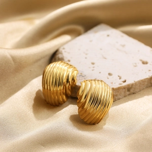 Macro detail of gold-plated croissant stud earrings on elegant travertine stone base