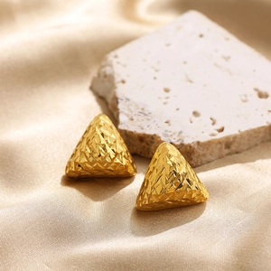 Macro view of 18K gold triangular stud earrings with geometric textured finish on silk