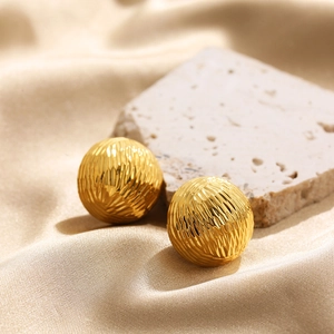 Detail of 18K gold stainless steel ball earrings with radiated texture on silk fabric