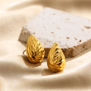 Close-up of golden geometric teardrop earrings with textured diamond-cut finish on silk