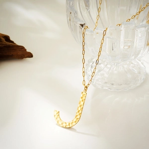 Macro shot of hammered gold letter J pendant with minimalist paperclip link chain