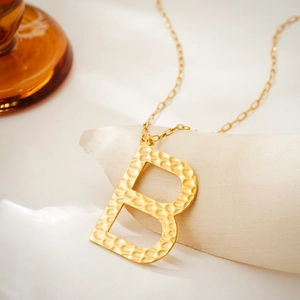 Macro shot of gold initial B pendant with hammered texture and fine metal chain