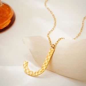 Macro detail of golden letter J pendant featuring a unique hammered texture finish