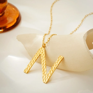 Detailed close-up of golden letter N pendant with hammer texture on chunky flat chain