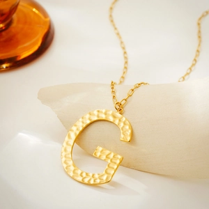 Detail of gold letter G pendant with hammered texture and oval link chain