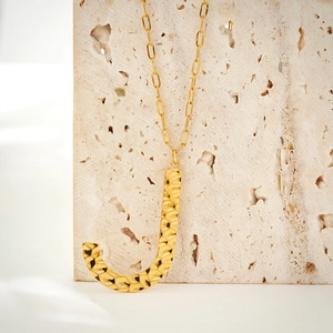 Macro shot of hammered gold letter J pendant on a trendy paperclip chain necklace