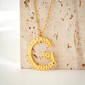 Detailed view of hammered gold letter G pendant necklace on minimalist chain link