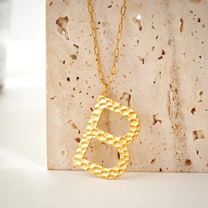 Detailed view of golden initial B pendant with hammered texture on paperclip link chain