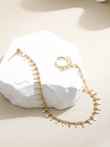Détail d'un earcuff doré avec chaîne à maillons et petites pastilles en métal texturé