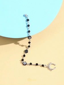 Détail macro du clip d'oreille punk avec perles noires et pendentifs fleurs sur chaîne