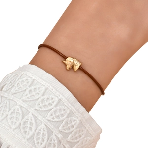 Detail of golden unicorn charm on dark brown cord bracelet with white lace cuff