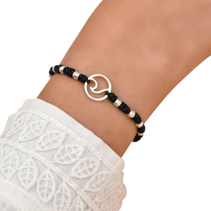 Detail of woven black rope bracelet with silver ocean wave charm on a female wrist