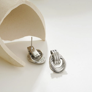 Detailed view of 18K gold-silver layered intertwined hoop earrings on minimalist ceramic