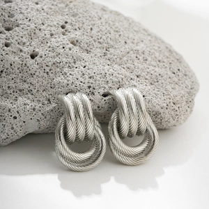 Macro shot of silver twisted knot stud earrings on textured grey volcanic rock display
