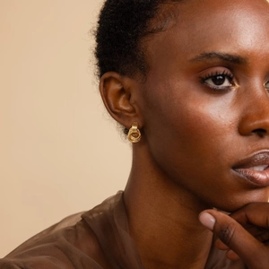 Close-up of 18K gold intertwined triple loop hoop earrings worn by a female model