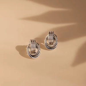 Macro detail of silver intertwined triple-hoop earrings with polished metallic mirror finish