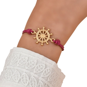 Close-up of golden ship wheel pendant with rose pink braided cord on female wrist