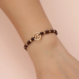 Detail of a brown woven cord bracelet with a gold wave charm and multifaceted beads