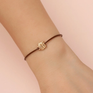 Detailed close-up of a golden owl charm on a slim brown cord bracelet worn on a wrist
