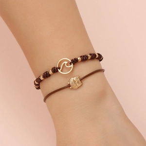 Minimalist leather rope bracelet set with woven band and golden owl charm on pink background