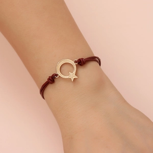 Close-up of red cord bracelet with gold moon and star charms worn on a model's wrist