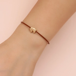 Close-up of a brown cord bracelet featuring a gold-toned unicorn charm on a person's wrist