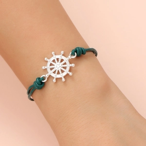 Close-up of green leather cord bracelet featuring a silver nautical helm steering wheel