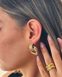 Detail of gold spiral knot earrings and chunky polished rings worn by a model