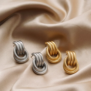 Close-up of twisted 18K gold and silver layered hoop earrings on champagne silk fabric