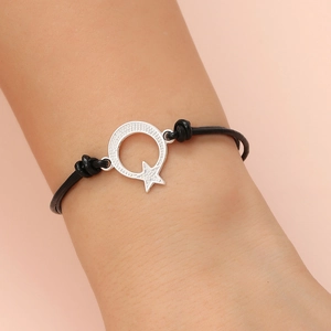 Detail of minimalist black leather cord bracelet featuring a silver star and moon charm
