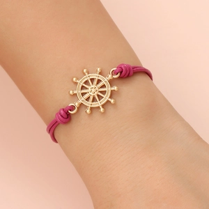 Detail of rose red leather cord bracelet with a golden nautical ship wheel charm