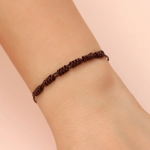 Close-up of a hand-woven dark brown leather cord bracelet with intricate knotting details