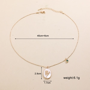 Dettaglio della collana ovale dorata con mughetto in madreperla e ciondolo in gemma verde