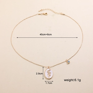 Dettaglio del ciondolo ovale dorato con motivo floreale e gemma blu su collana a catena