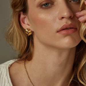 Close-up of geometric 18k gold triple-layered crossover stud earrings on a model