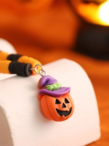 Makroaufnahme des Halloween-Kürbisanhängers mit lila Hexenhut an orange-schwarzer Perlenkette