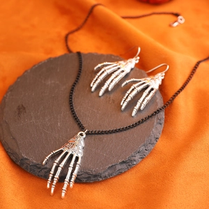 Detailansicht des silbernen Skeletthand-Schmucksets mit Halskette und Ohrringen auf Schiefer